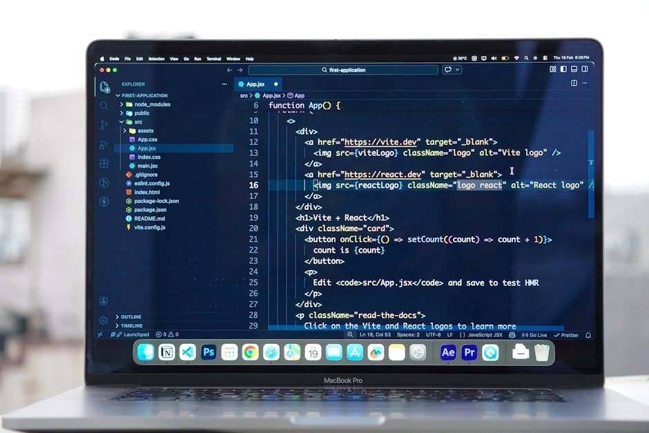 A person working on a laptop displaying a software coding interface with colorful lines of code on a dark background. The individual is seated at a desk with a black mug nearby, and their hands are po